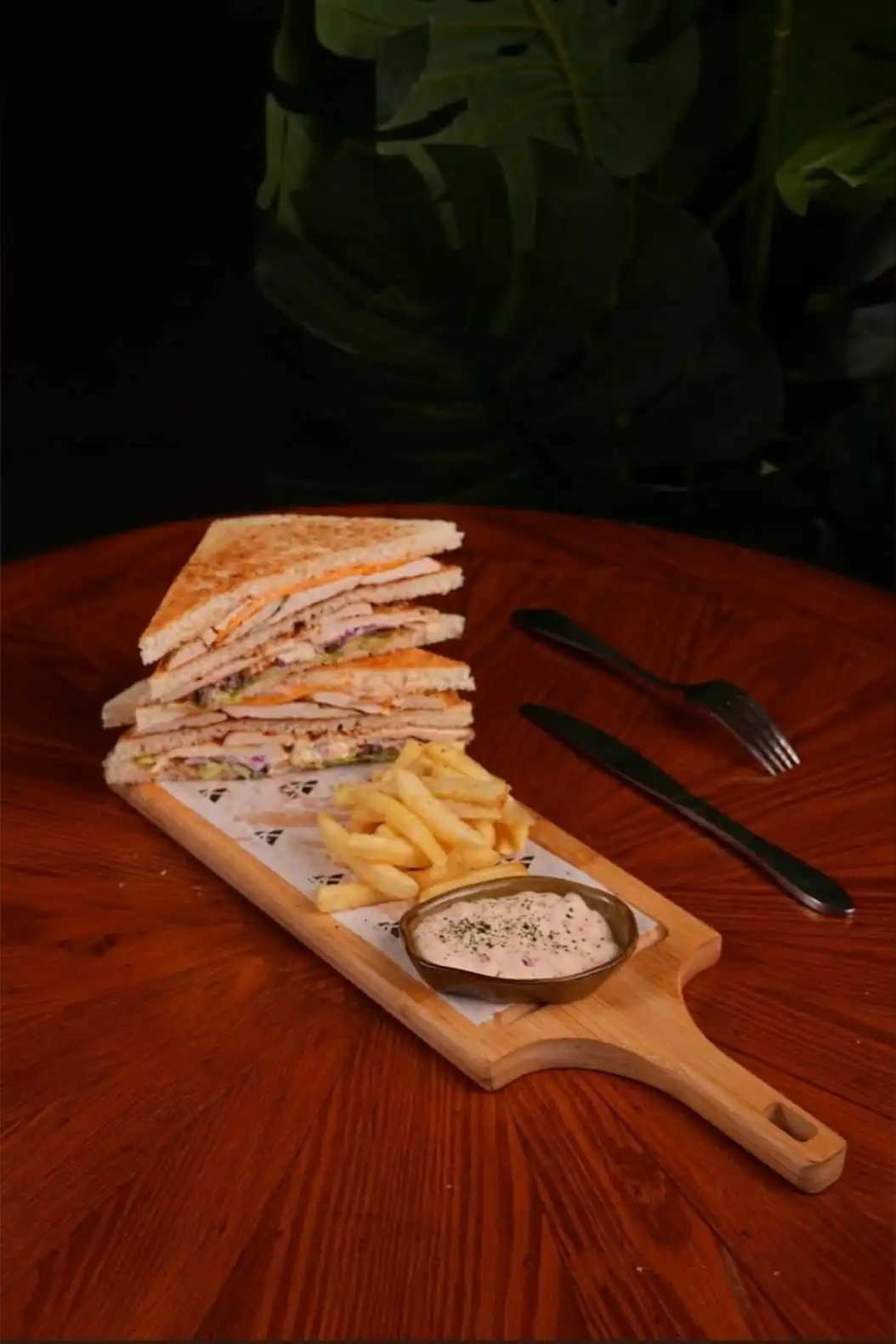 Stacked club sandwich with fries and dip on a wooden board