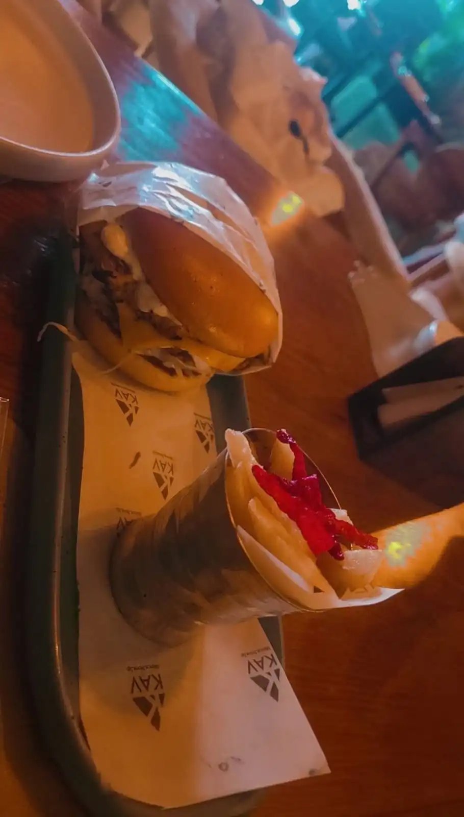 Two KAV-branded hot dogs in paper wrapping, served on a wooden board with KAV paper liner