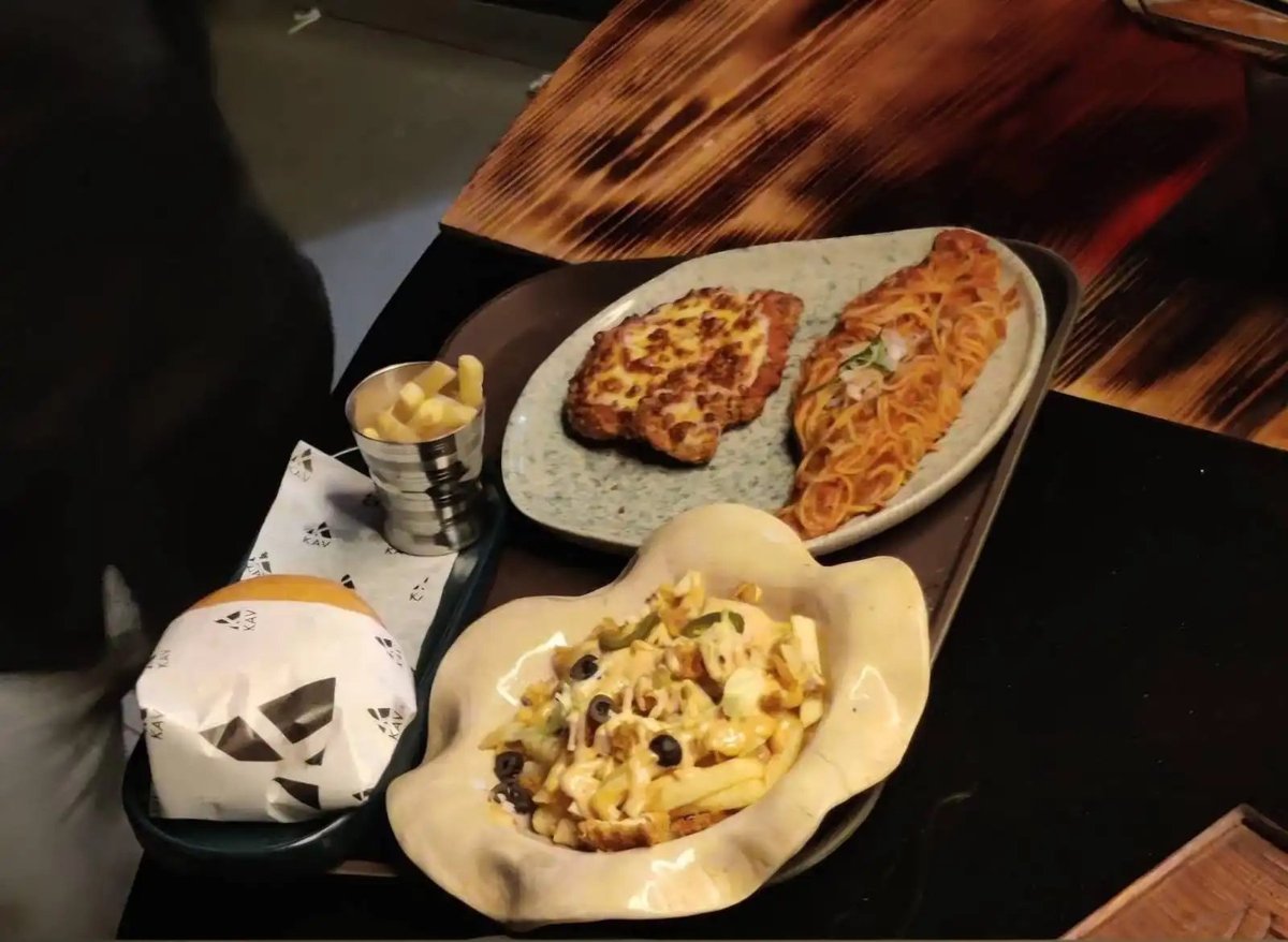 Overhead view of a KAV spread with two pizzas, a pasta dish, cheesy potatoes and dipping sauce on a wooden table