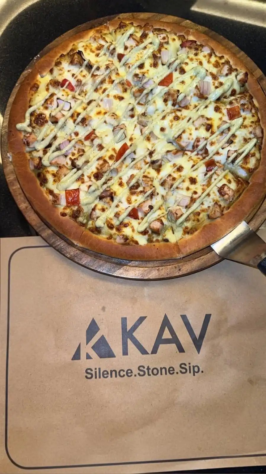 KAV meat-loaded pizza with bacon, ham and sausage drizzled in white sauce, served on the signature KAV stone pizza board with the Silence. Stone. Sip. tagline
