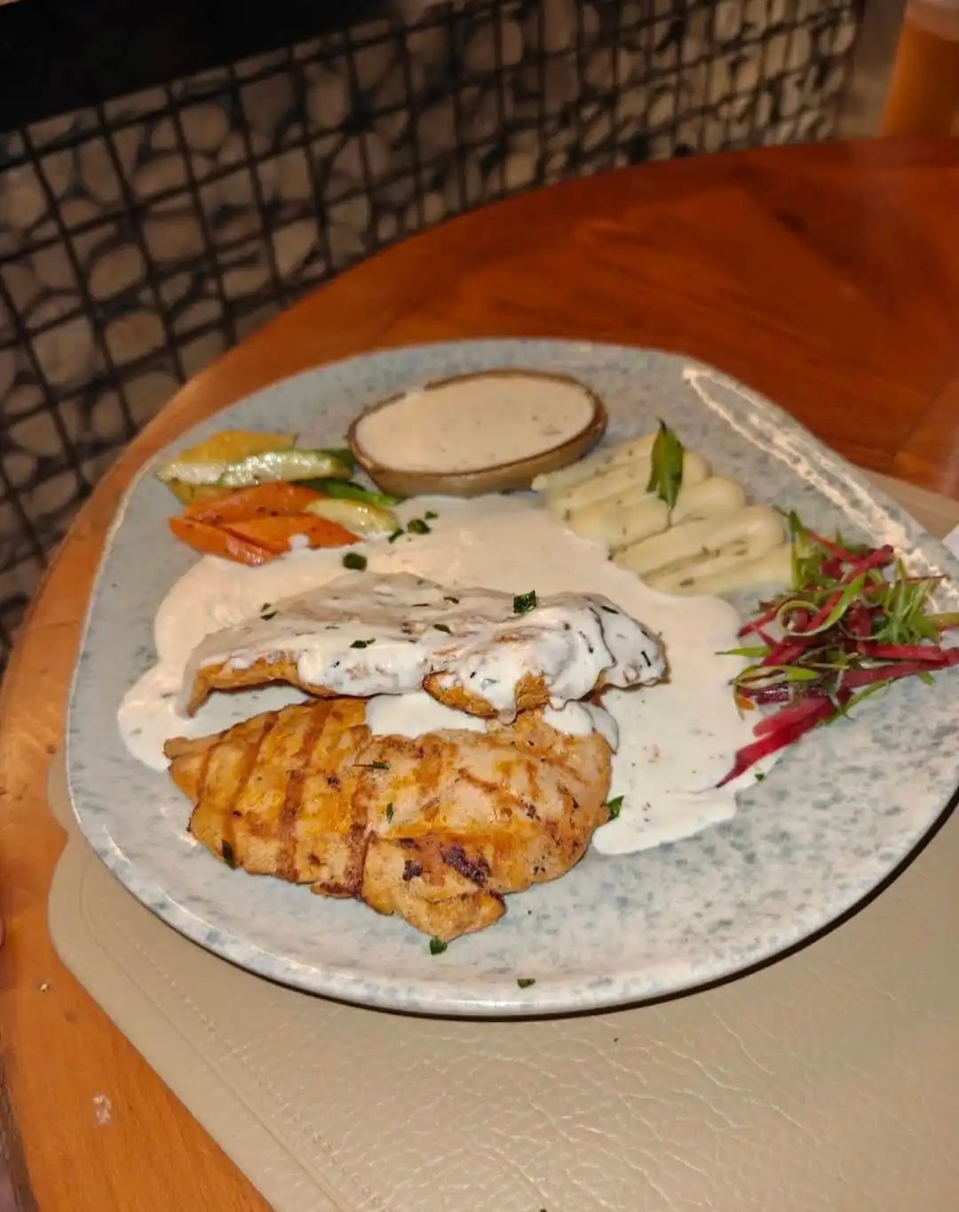 Gourmet chicken breast glazed in cream sauce, served on a white plate with mashed potatoes, baby corn, carrots, asparagus and beetroot slaw