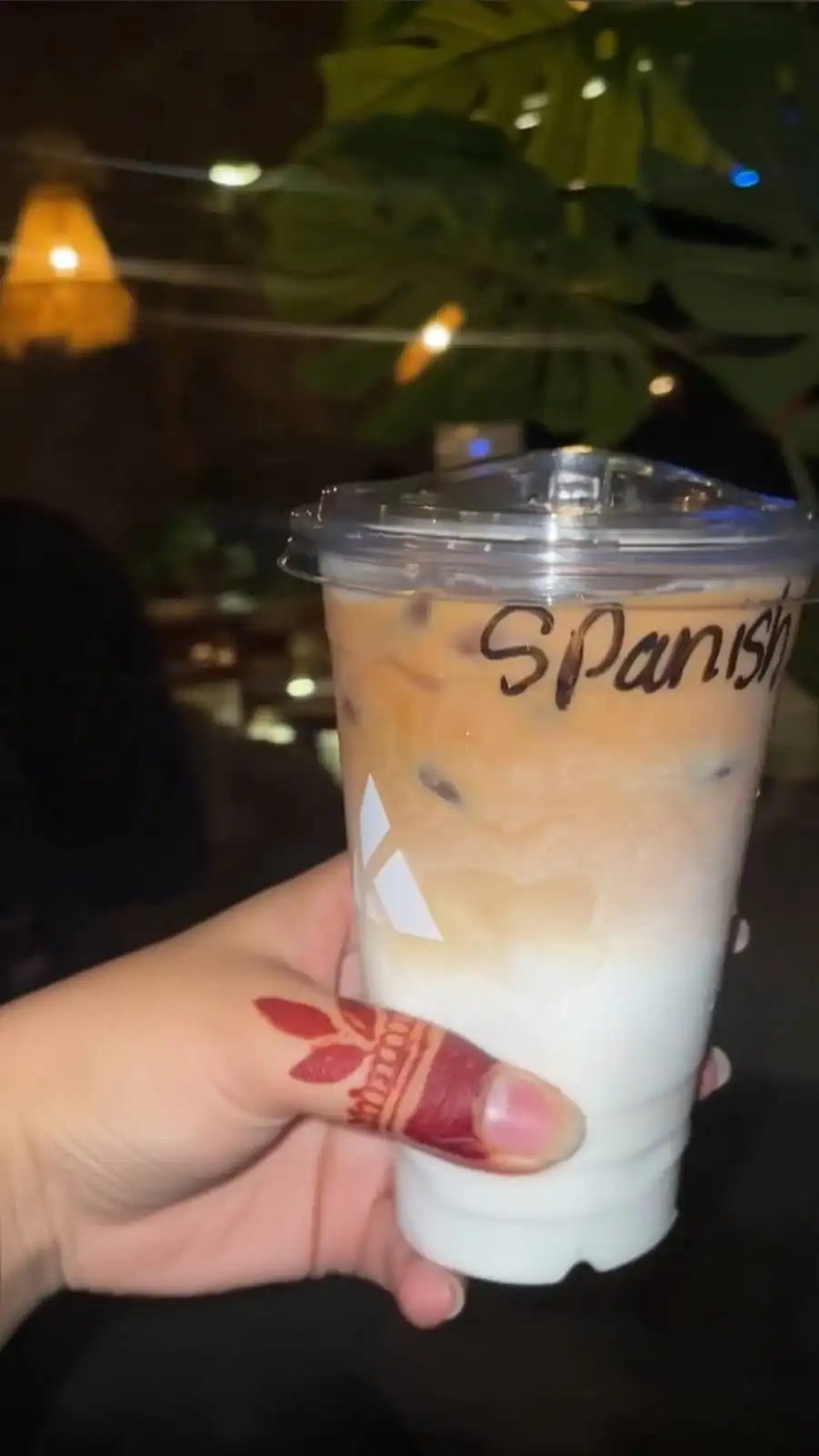 Hand holding a KAV branded Spanish latte with a layered coffee and milk drink in a clear plastic cup