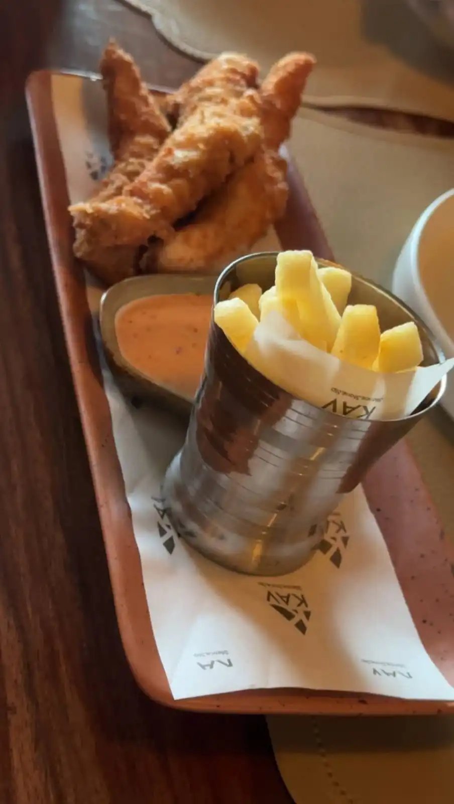 KAV fish and chips — golden fried fish fillets with thick-cut fries, served with a side of sauce on a wooden tray