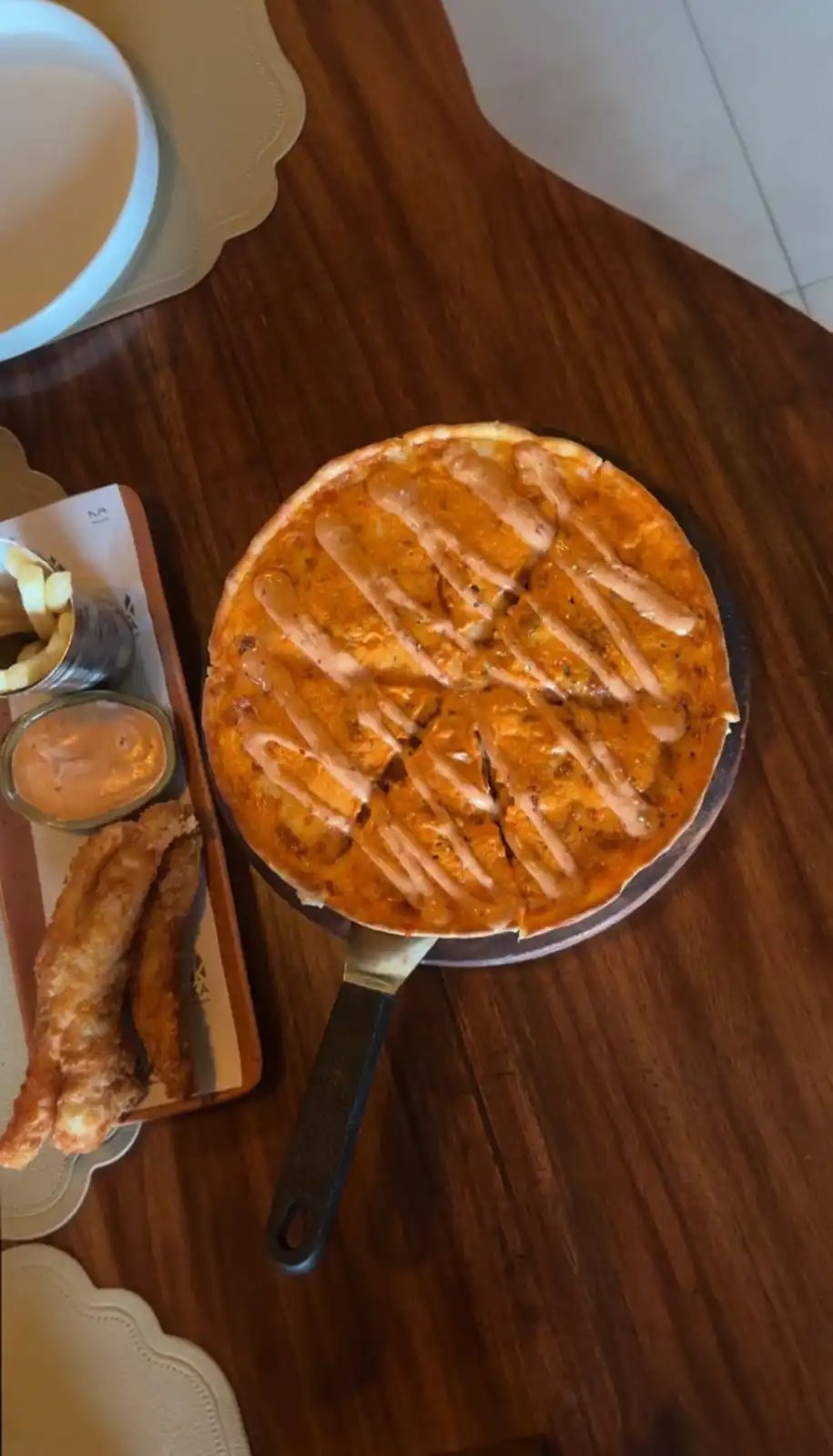 Overhead view of a skillet with a deep-dish KAV pizza drizzled with caramel sauce, served with breadsticks and dipping sauce