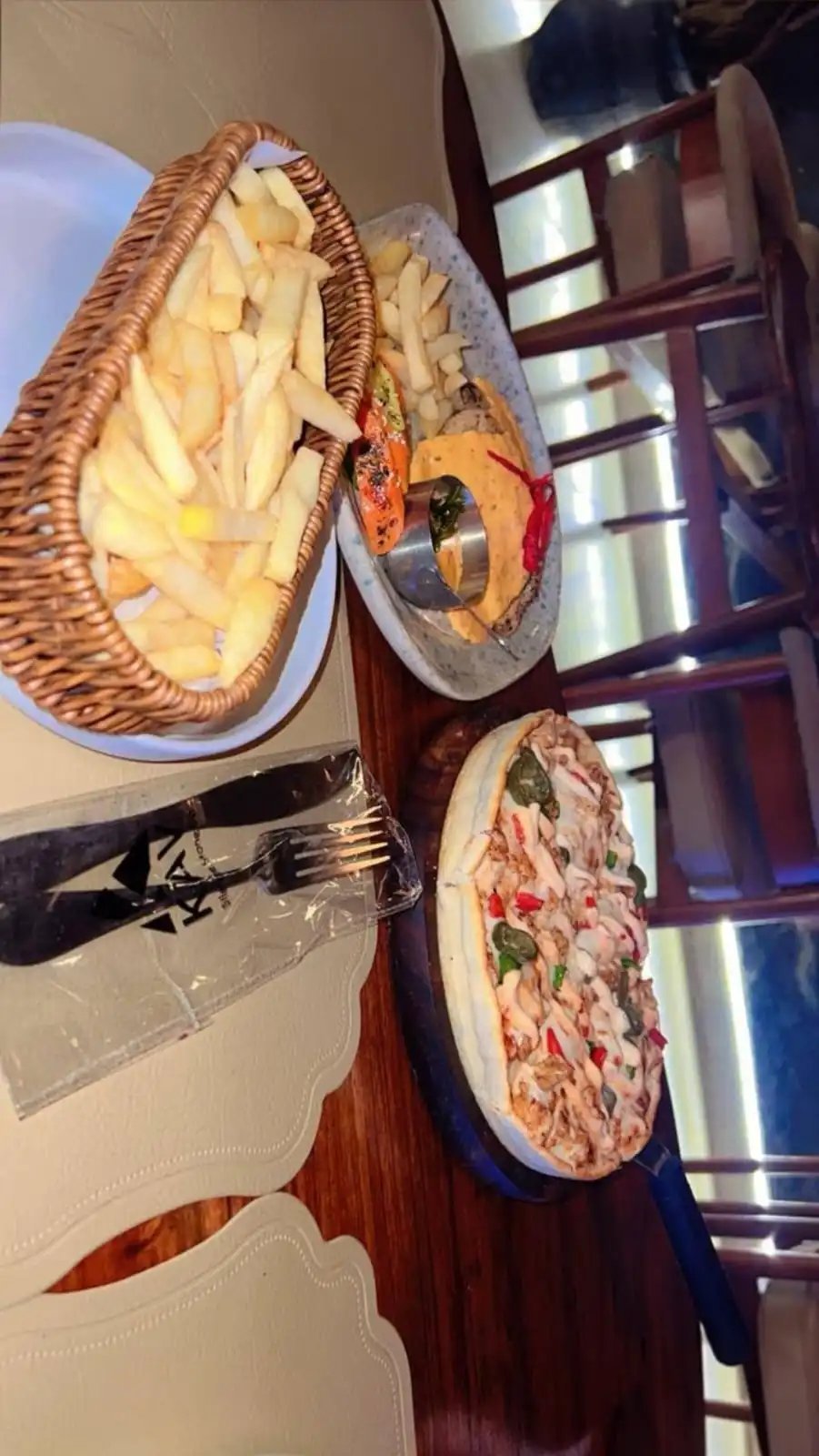 Assorted KAV sandwiches and fries displayed on plates and in a wicker basket on a wooden table