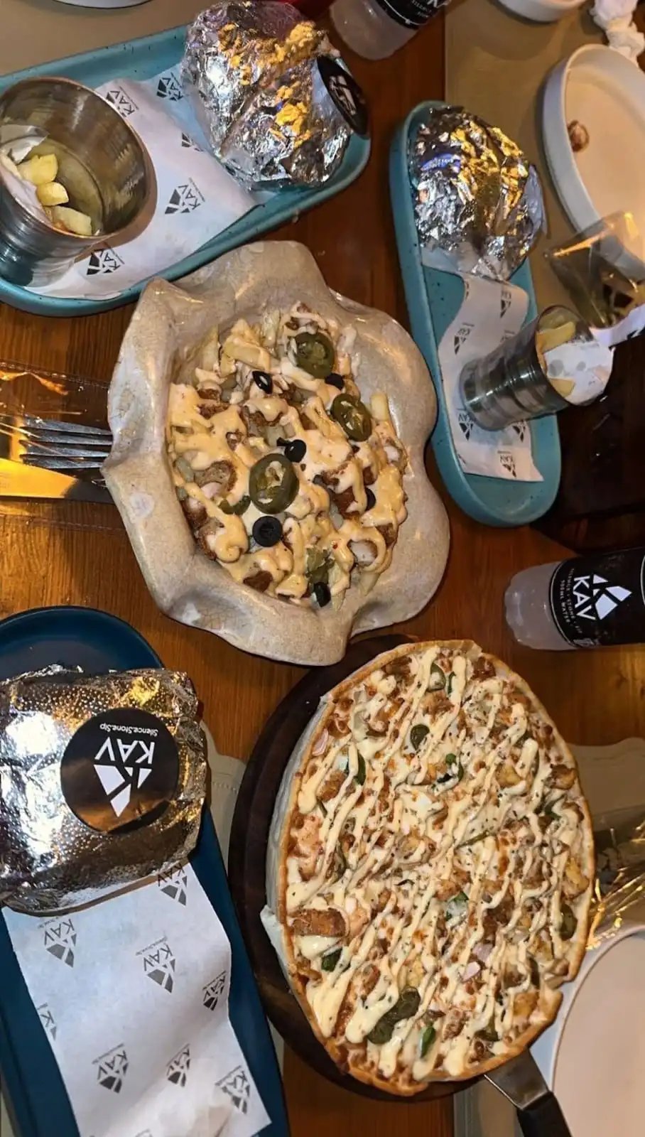 Overhead view of KAV pizzas and foil-wrapped items on branded blue trays during a meal